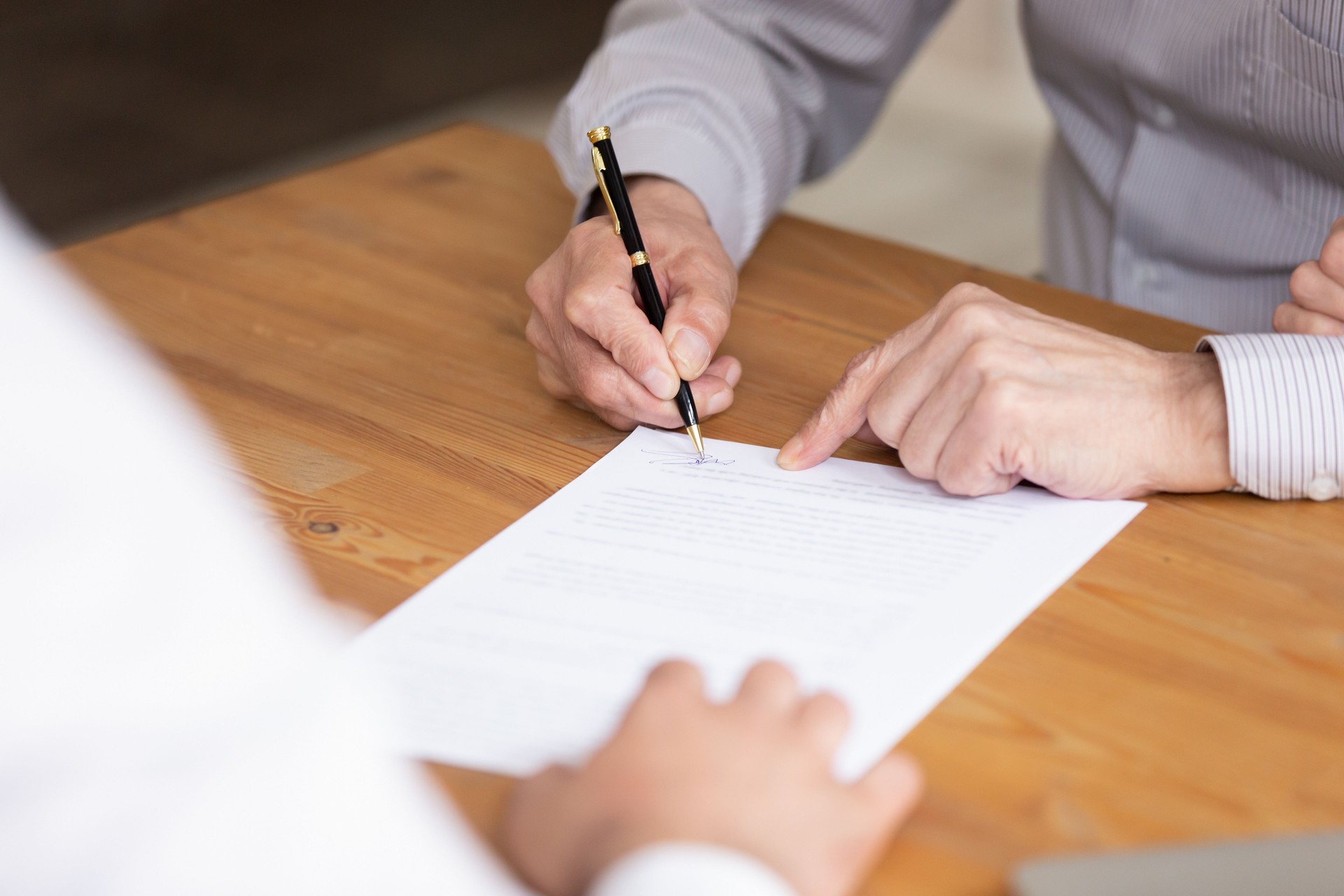 Elderly male hand signing document close up image